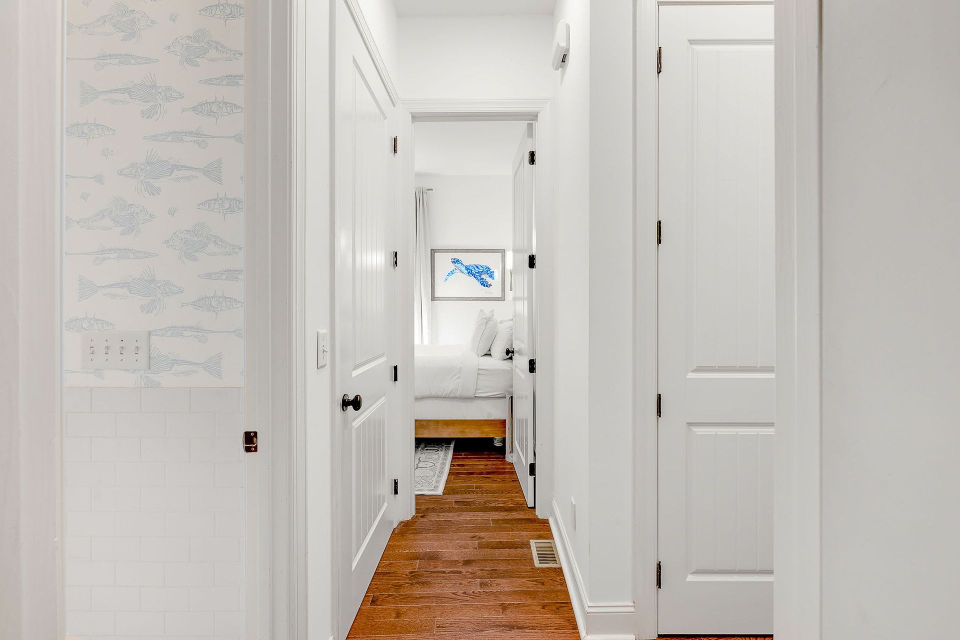 A hallway leading to a bedroom with hardwood floors and white walls.