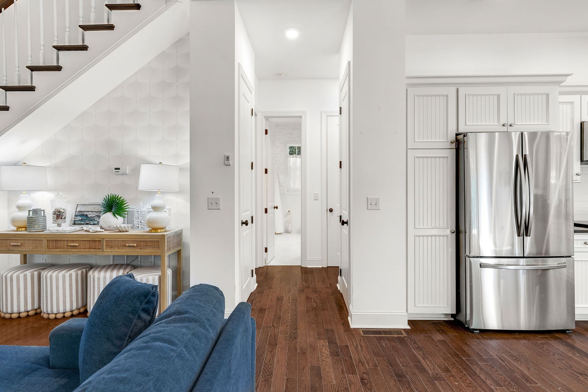 A living room with a blue couch and a stainless steel refrigerator.