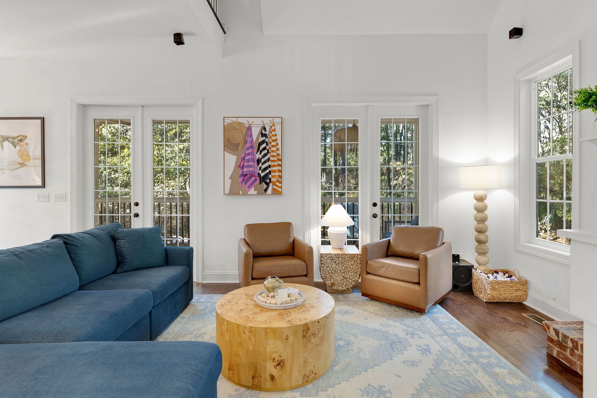 A living room with a blue couch , two chairs , a coffee table and a painting on the wall.