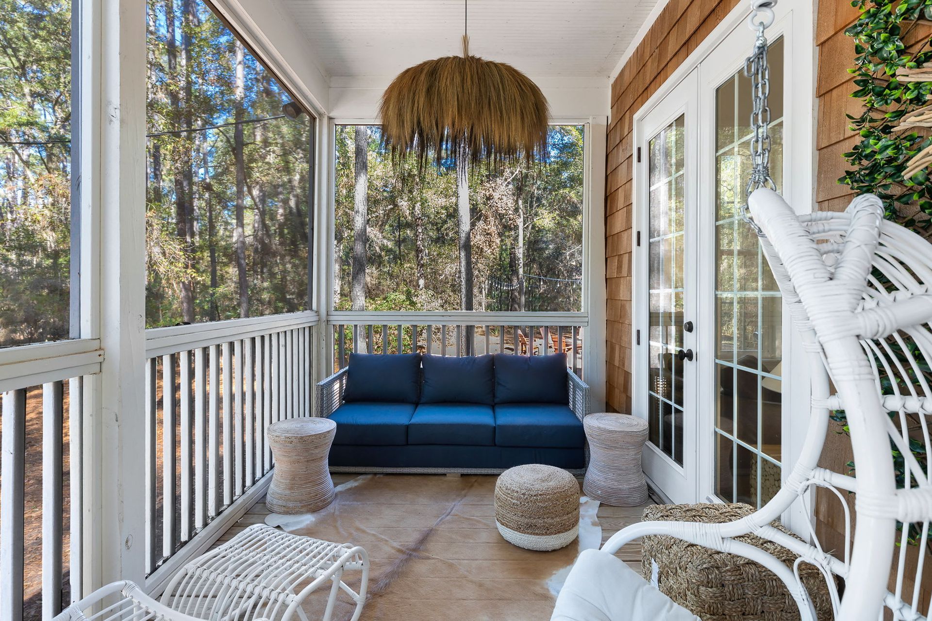 A screened in porch with a blue couch and white chairs.
