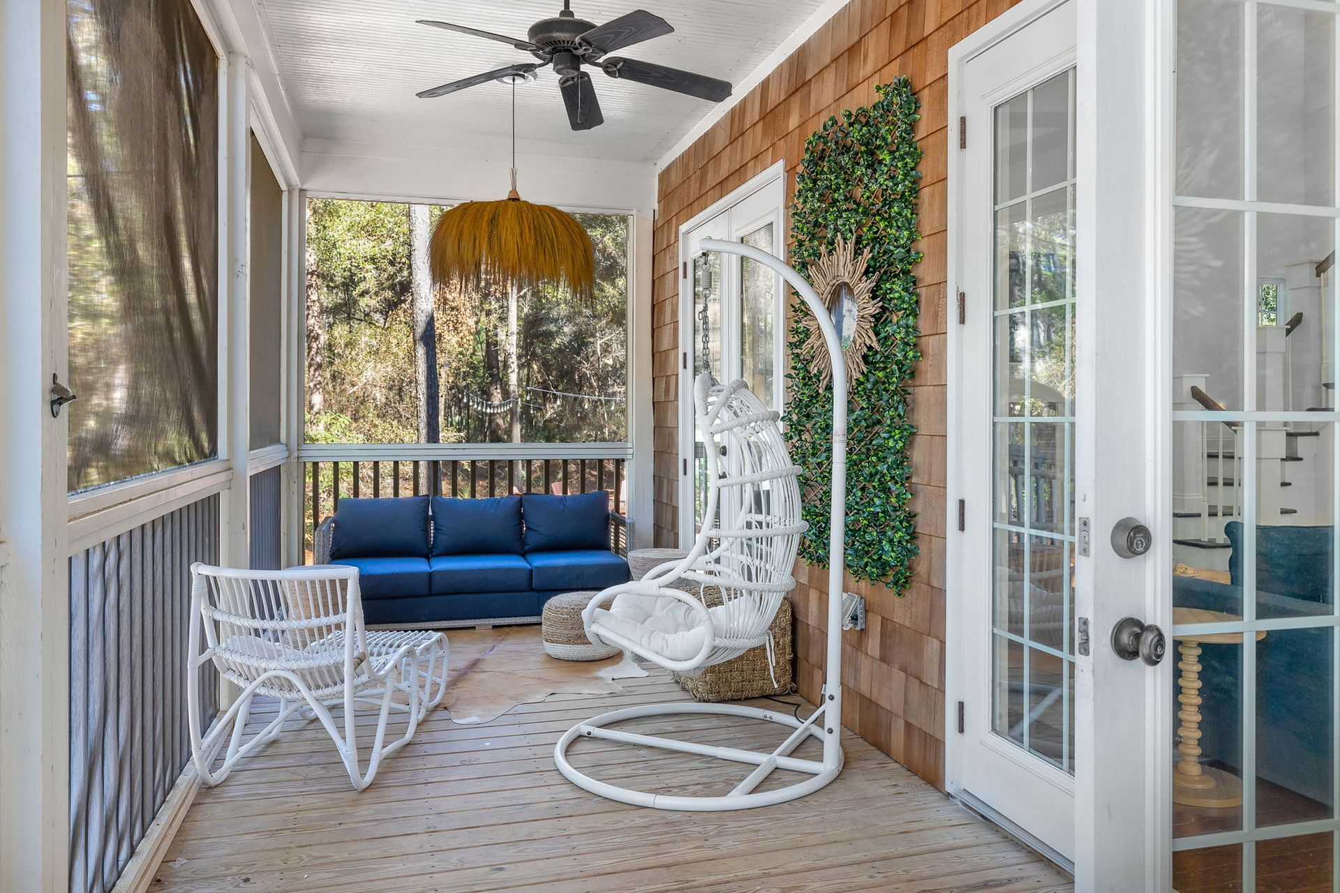 A screened in porch with a couch and chairs and a ceiling fan.