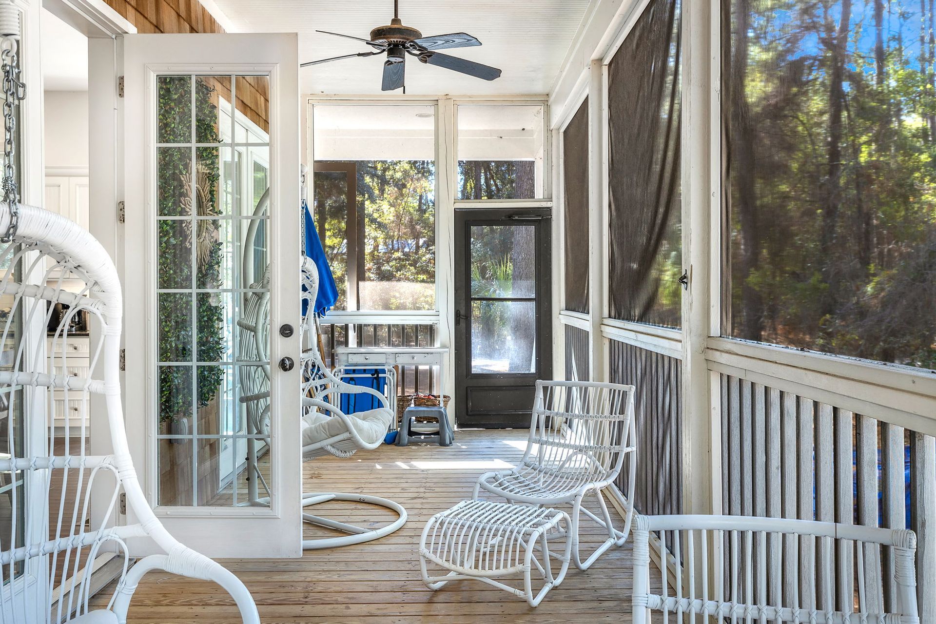 A screened in porch with white chairs and a ceiling fan.
