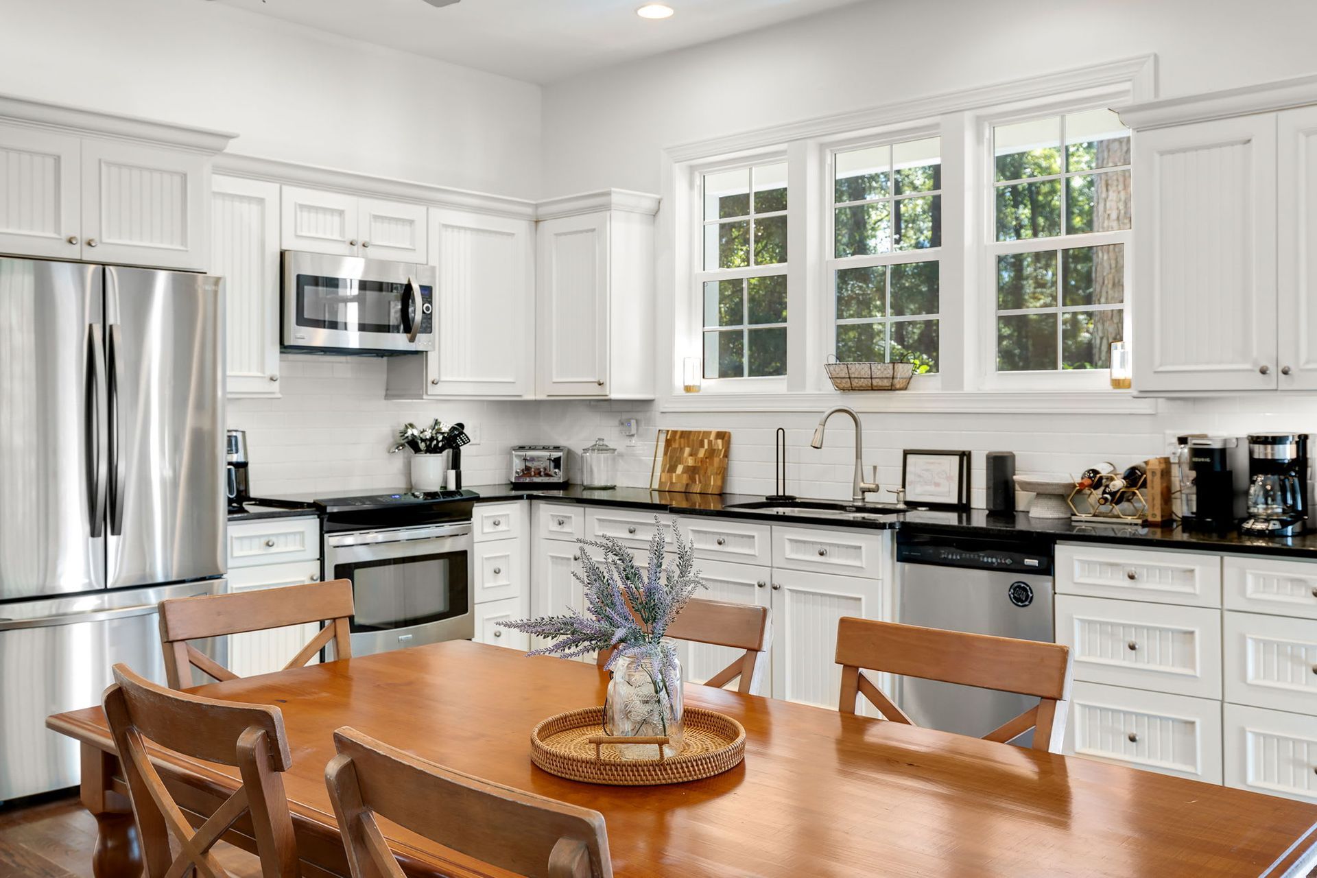 A kitchen with white cabinets , stainless steel appliances , a table and chairs.
