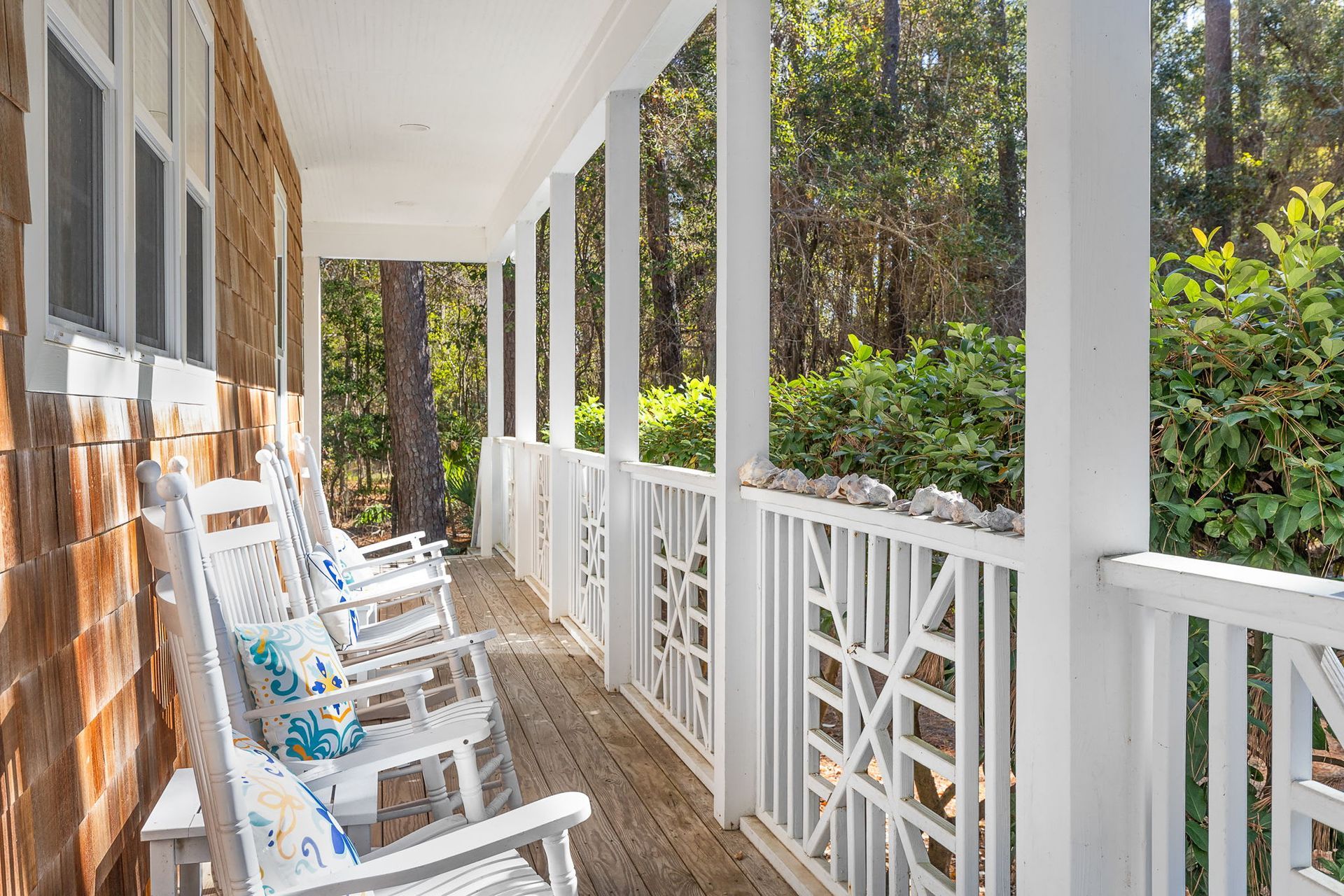 A porch with a row of white rocking chairs on it.