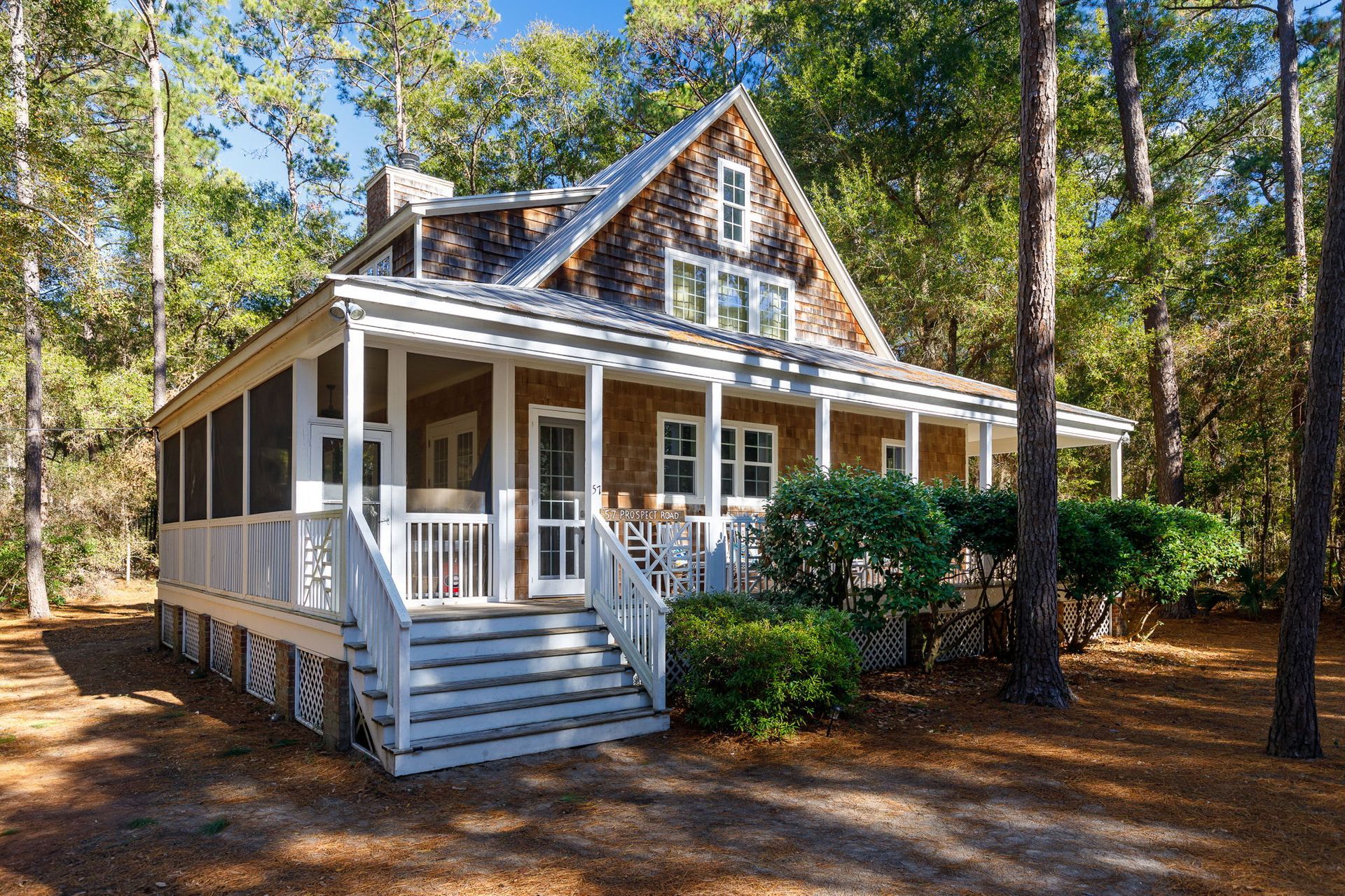 A small house with a screened in porch in the middle of a forest.