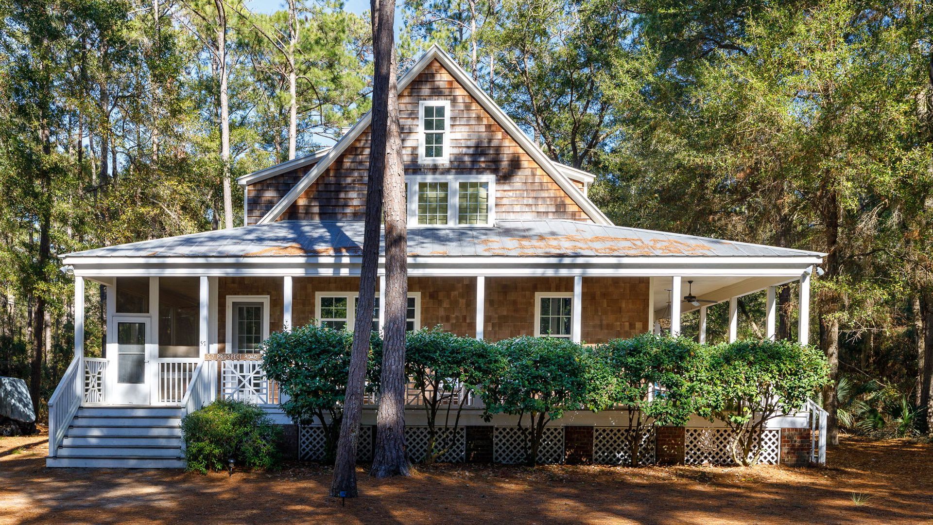 A large house with a large porch is surrounded by trees.