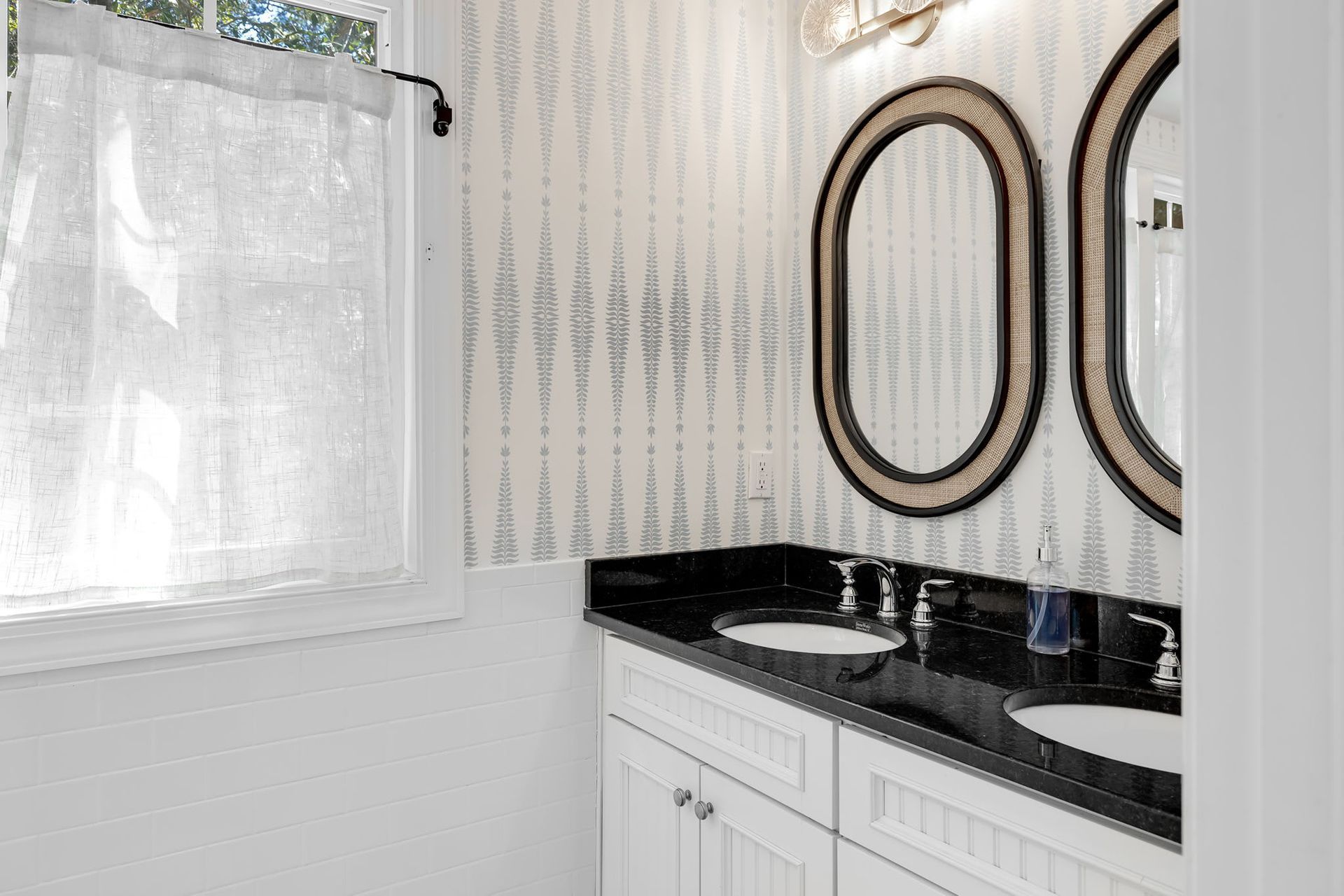 A bathroom with two sinks , two mirrors and a window.