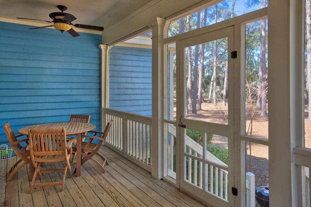 A screened in porch with a table and chairs and a ceiling fan