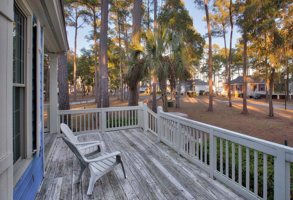 A wooden deck with chairs and a white railing surrounded by trees.