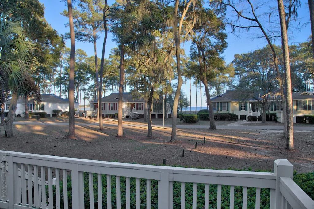A white fence surrounds a yard with trees and houses in the background.