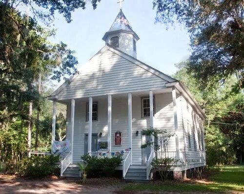 A white church with a steeple is surrounded by trees