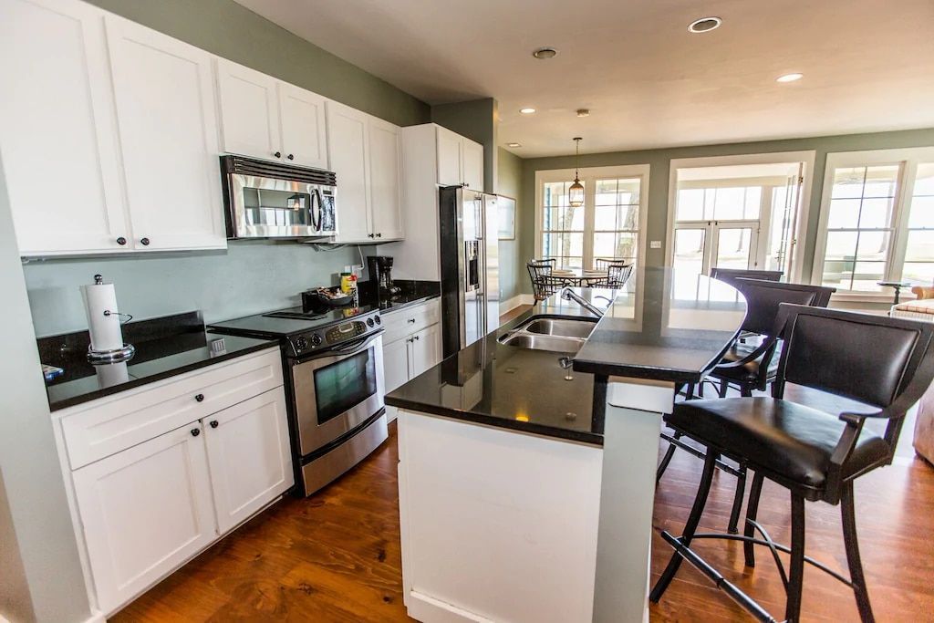 A kitchen with white cabinets , black counter tops , stainless steel appliances and a large island.
