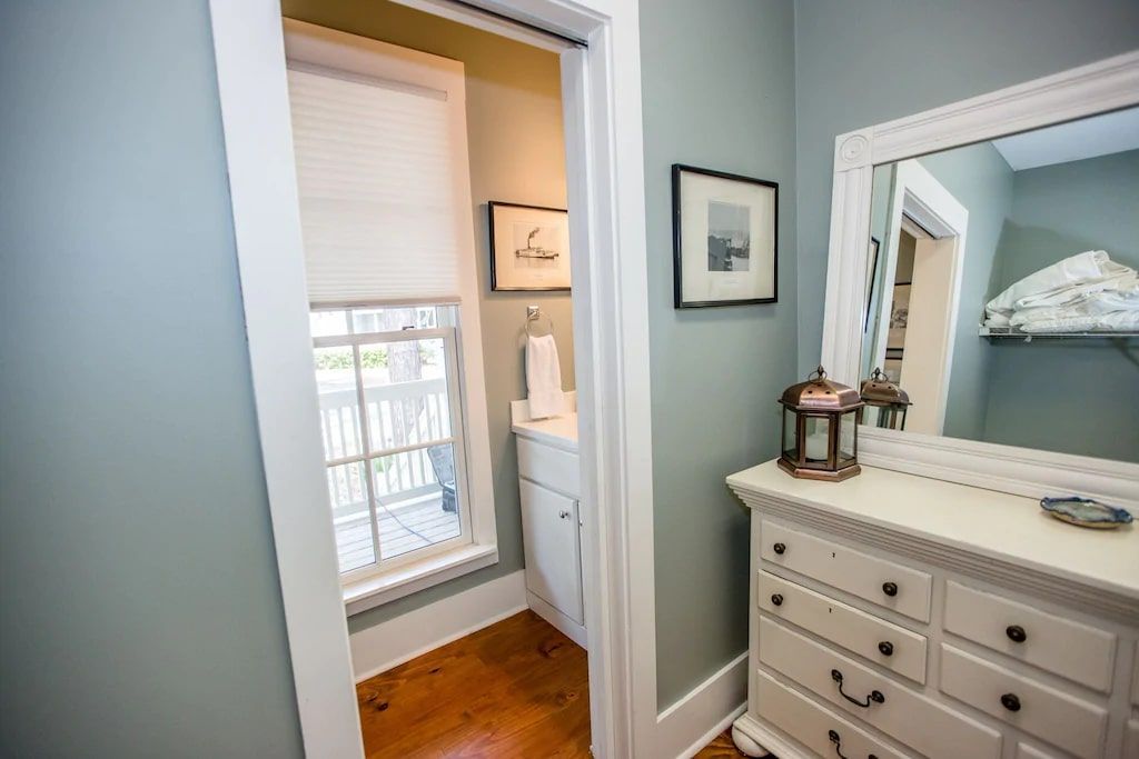 A bedroom with a dresser , mirror and window.