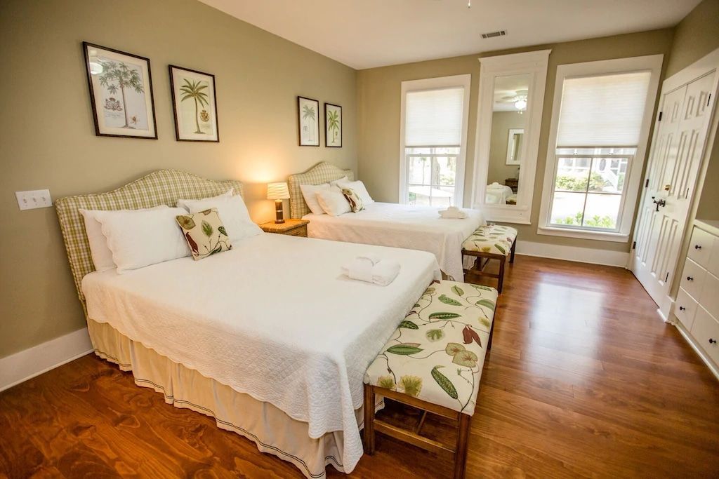 A bedroom with two beds , a bench and a mirror.