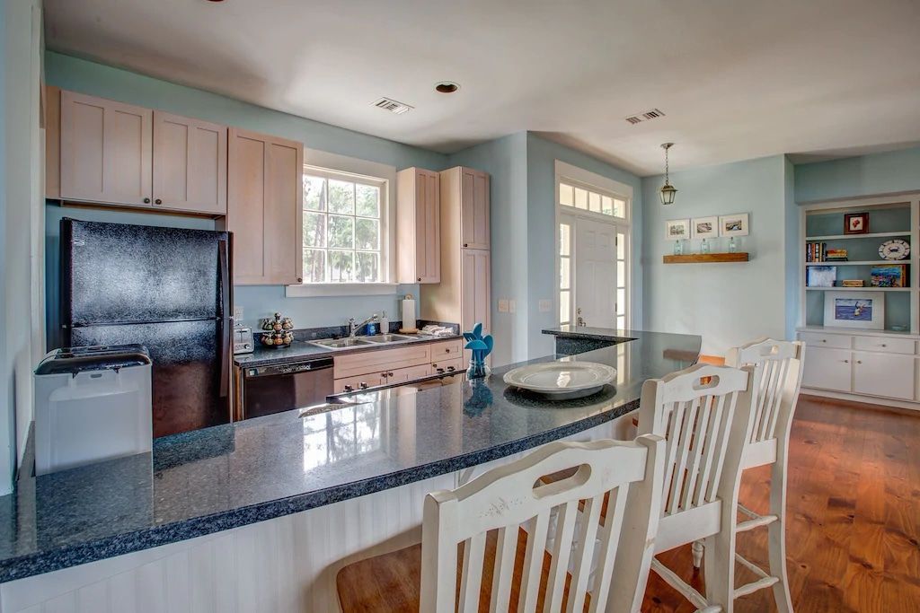 A kitchen with a large island , stools , and a refrigerator.