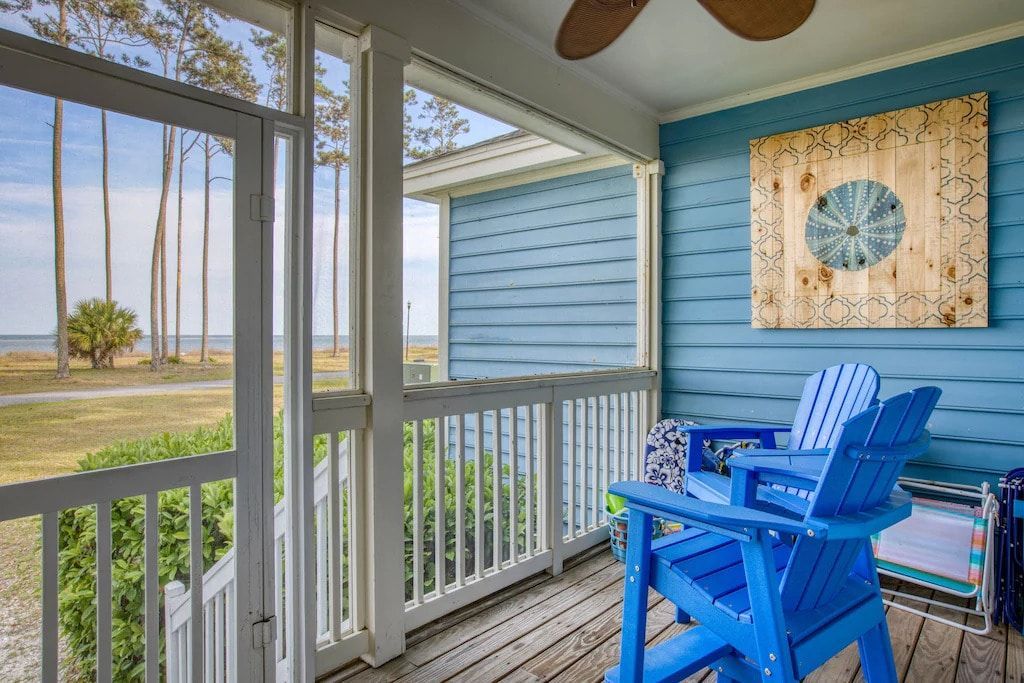 A screened in porch with two blue chairs and a ceiling fan.