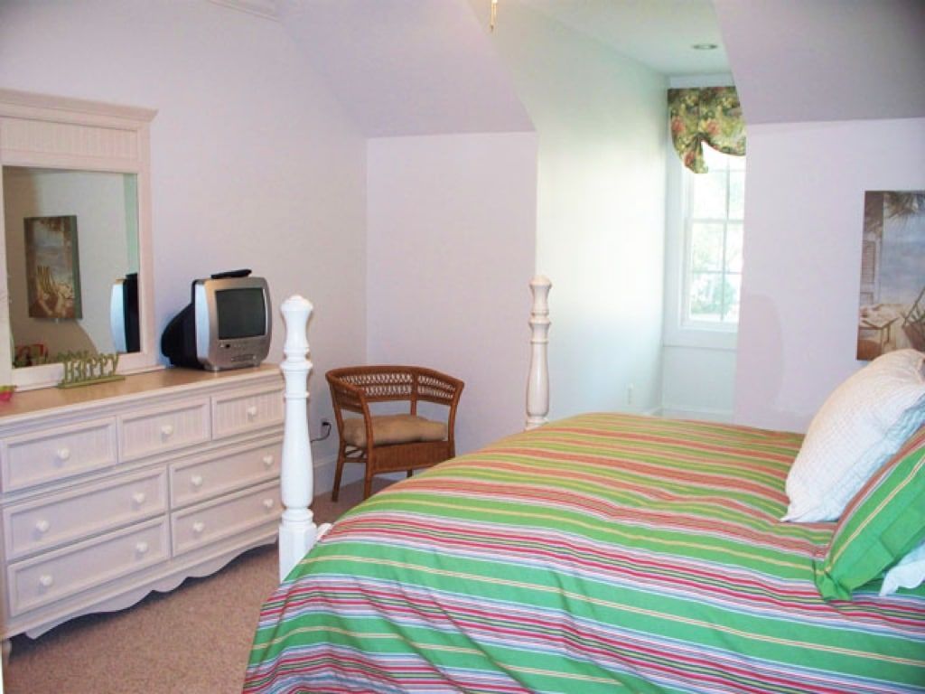 A bedroom with a bed , dresser , chair and television.