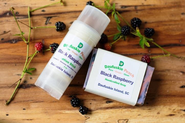 A bottle of lip balm and a bar of black raspberry soap on a wooden table.