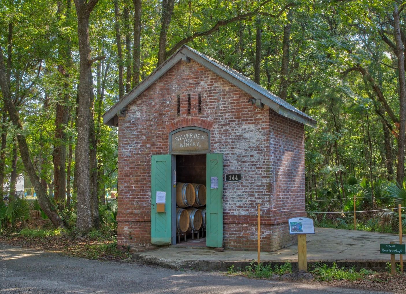 A small brick building with barrels inside of it is surrounded by trees.