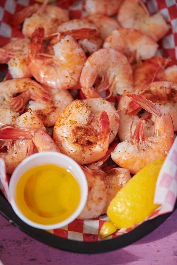 A basket of shrimp with a cup of oil and a lemon slice.