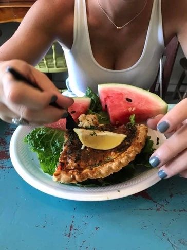 A woman is eating a sandwich with watermelon and lettuce on a paper plate.