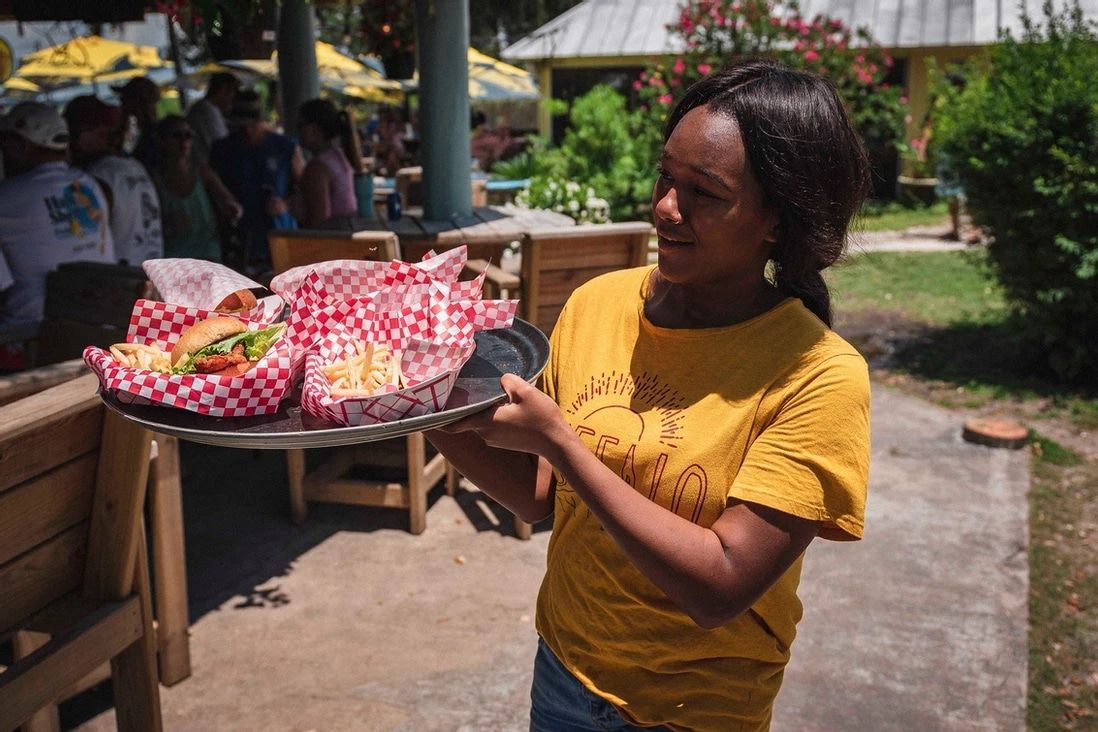 A woman in a yellow shirt is holding a tray of food.
