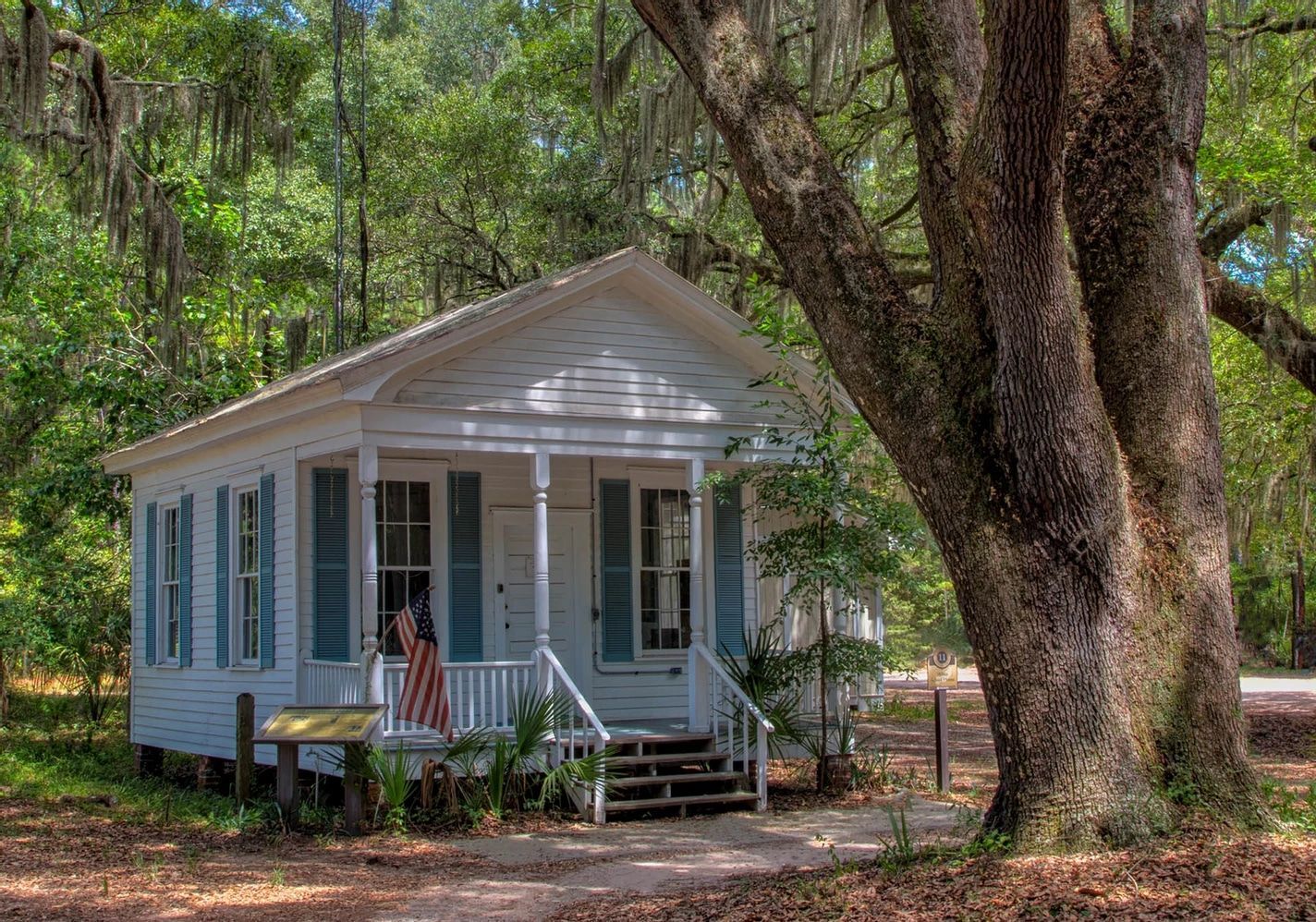 A small white house with blue shutters is surrounded by trees.
