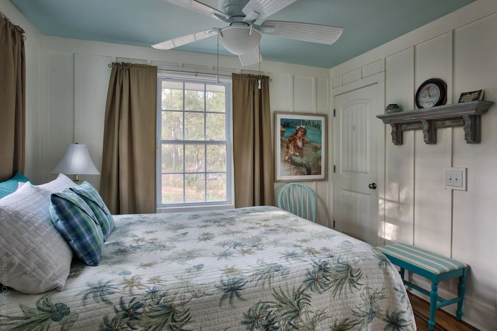 A bedroom with a king size bed , a ceiling fan , a window and a bench.