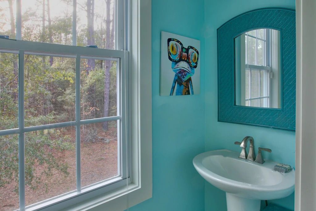A bathroom with blue walls , a sink , a mirror and a window.