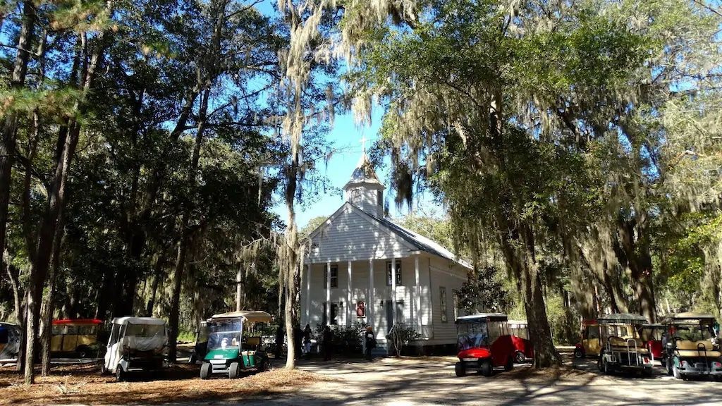 A group of golf carts are parked in front of a church surrounded by trees.
