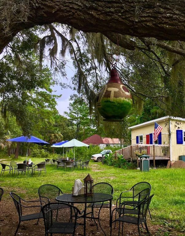 A christmas ornament hangs from a tree in a yard with tables and chairs