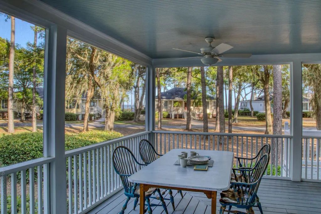 A screened in porch with a table and chairs and a ceiling fan.