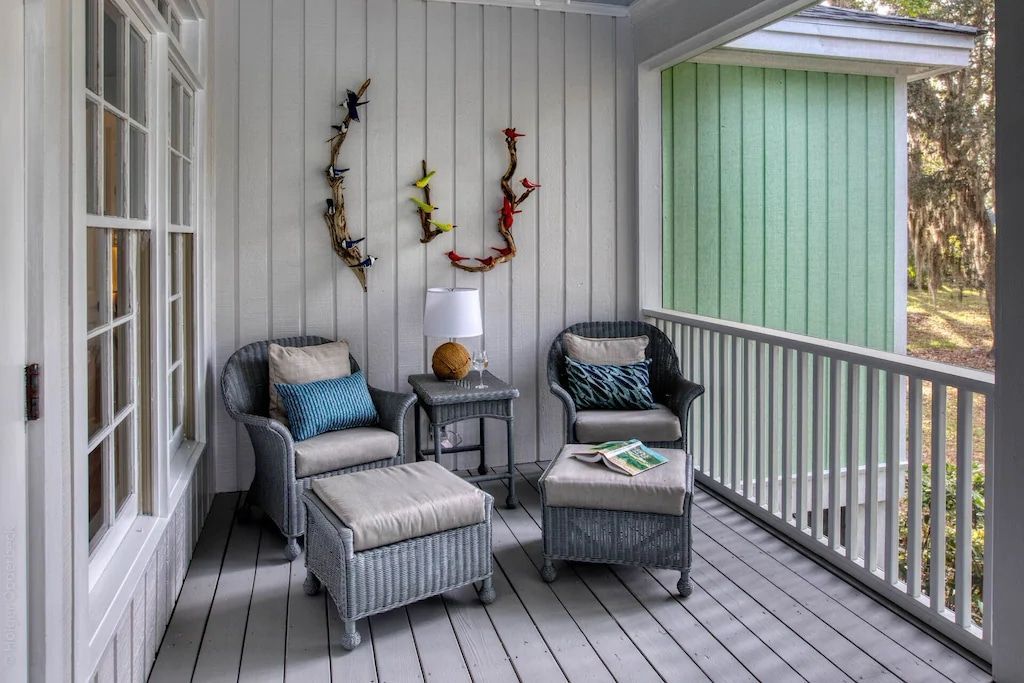 A porch with wicker chairs and ottomans and a green wall.