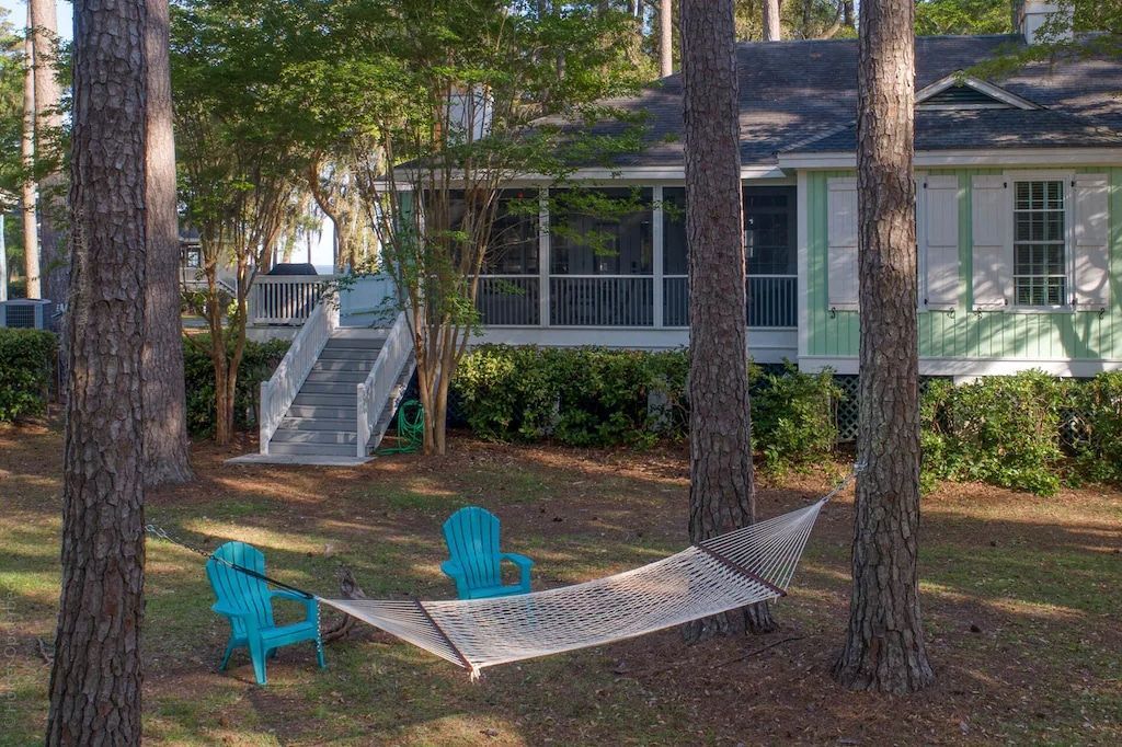 A hammock is hanging between two trees in front of a house.