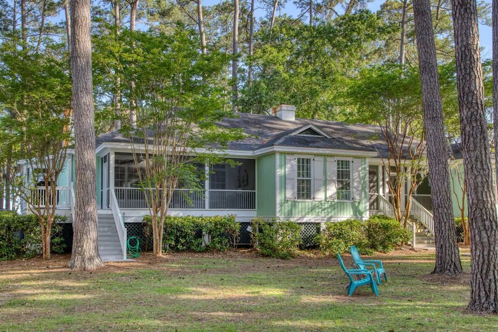 A green house with a blue chair in front of it is surrounded by trees.