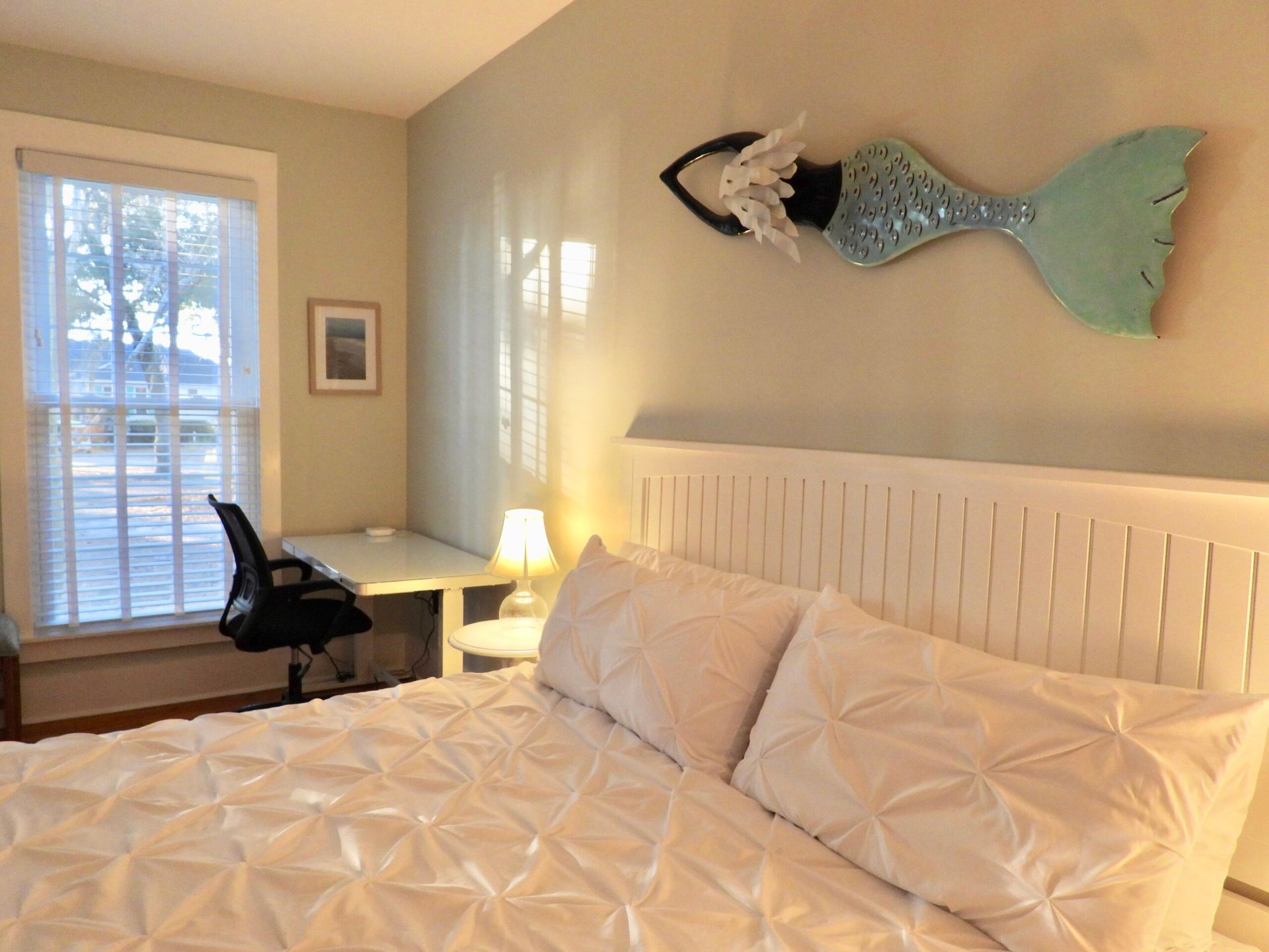 A bedroom with a bed , desk , chair and a fish on the wall.