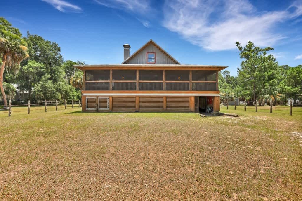 A white house with a screened in porch is surrounded by trees and bushes.