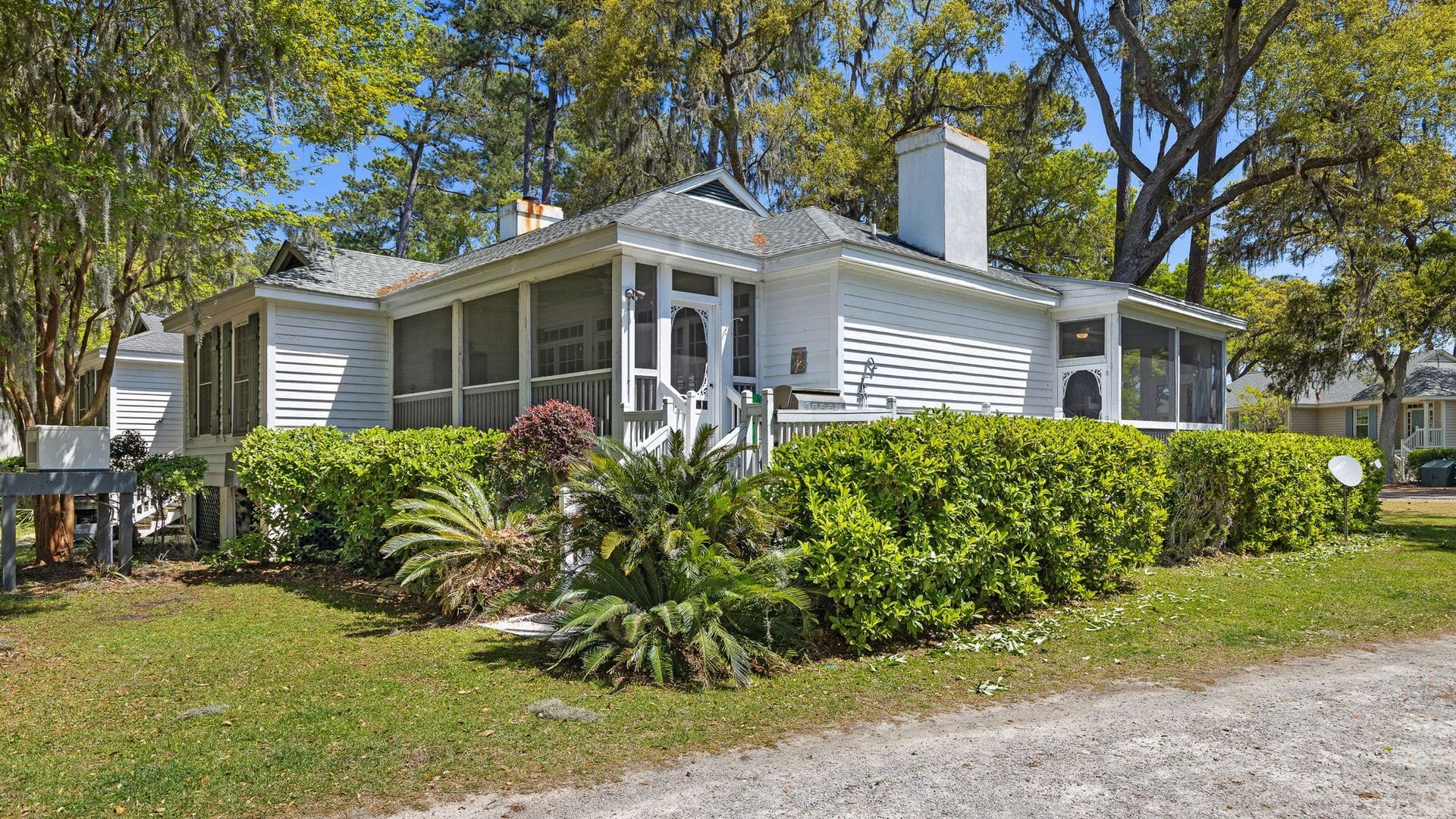 A white house with a screened in porch is surrounded by trees and bushes.