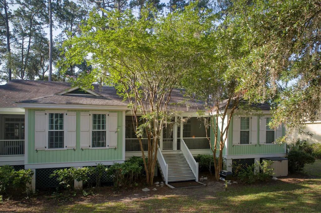 A green house with white shutters and trees in front of it