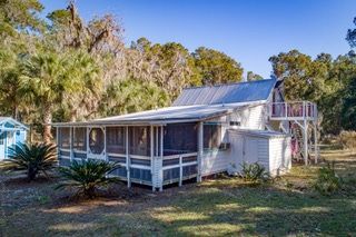A white house with a screened in porch is surrounded by trees.