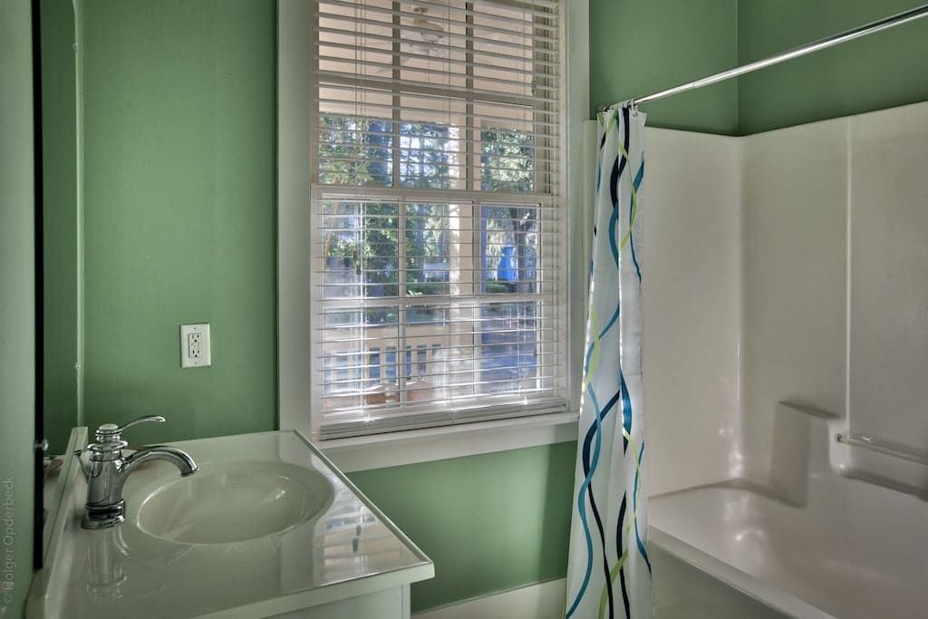 A bathroom with green walls , a sink , a tub and a window.