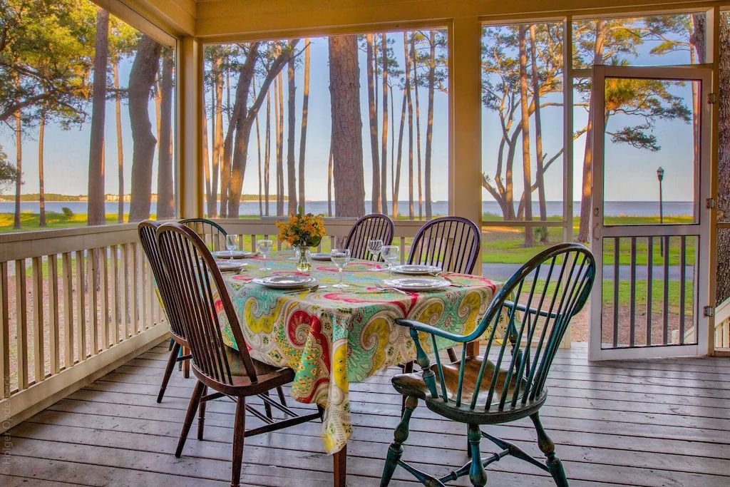 A screened in porch with a table and chairs and a view of the ocean.