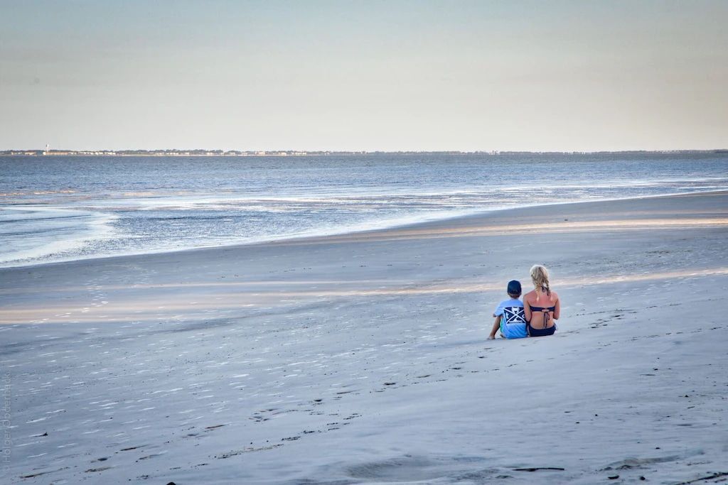 Two people are sitting on the beach looking at the ocean.