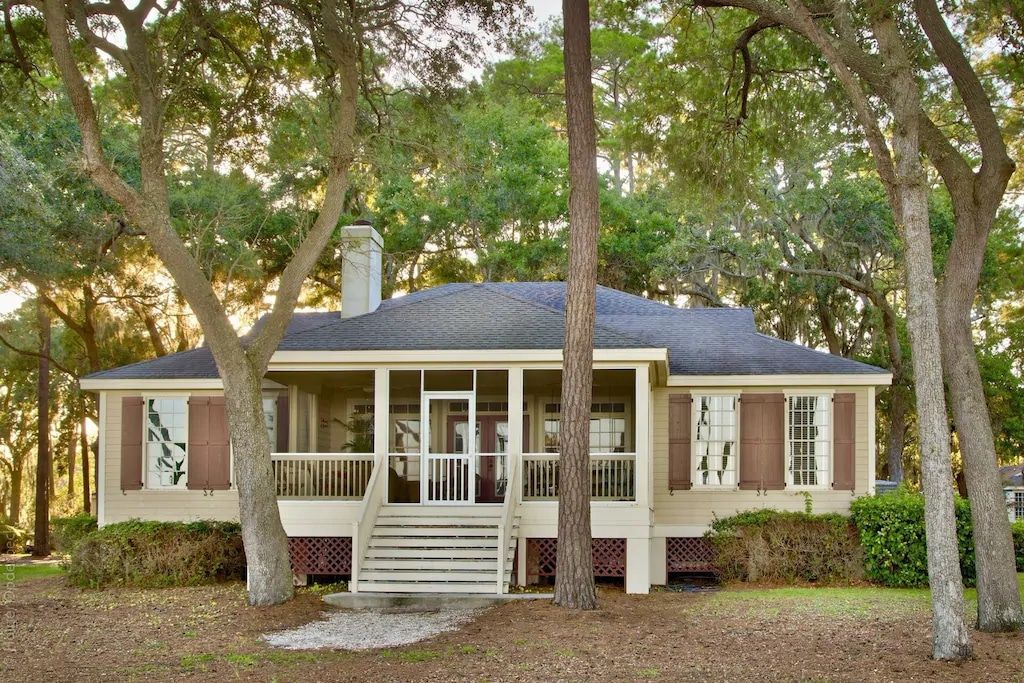 A house with a screened in porch is surrounded by trees.