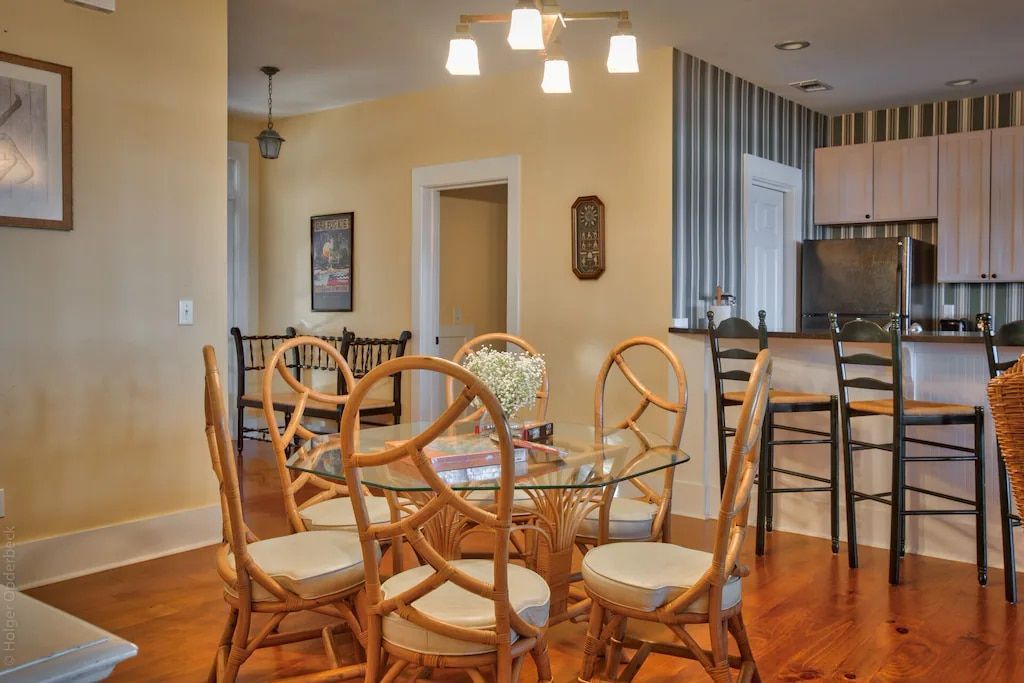 A dining room with a table and chairs and a kitchen in the background.