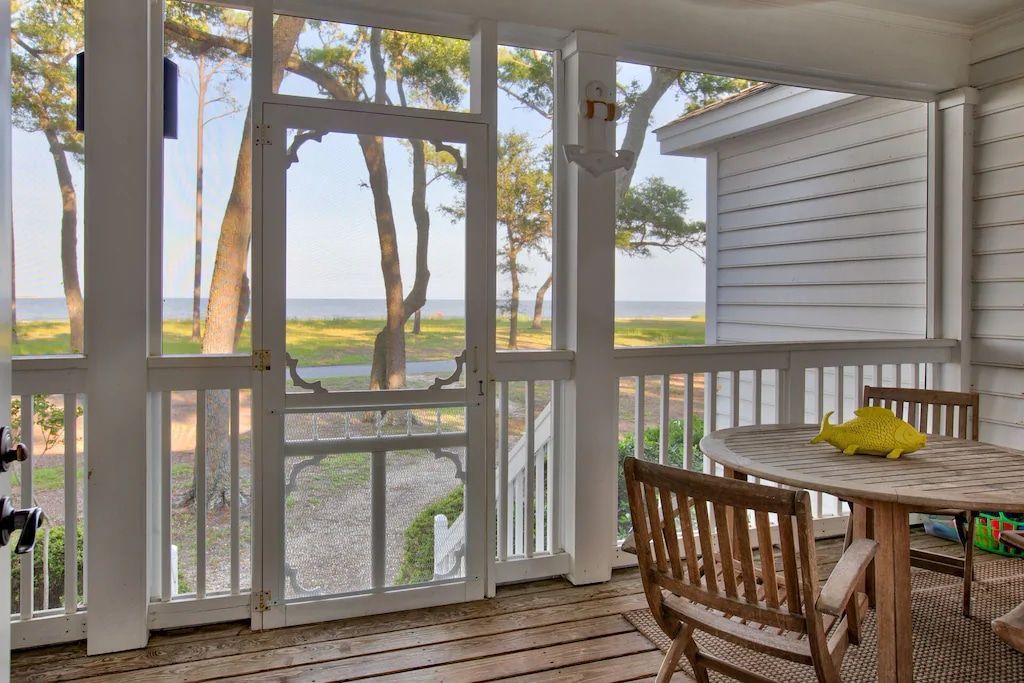 A screened in porch with a table and chairs and a view of the ocean