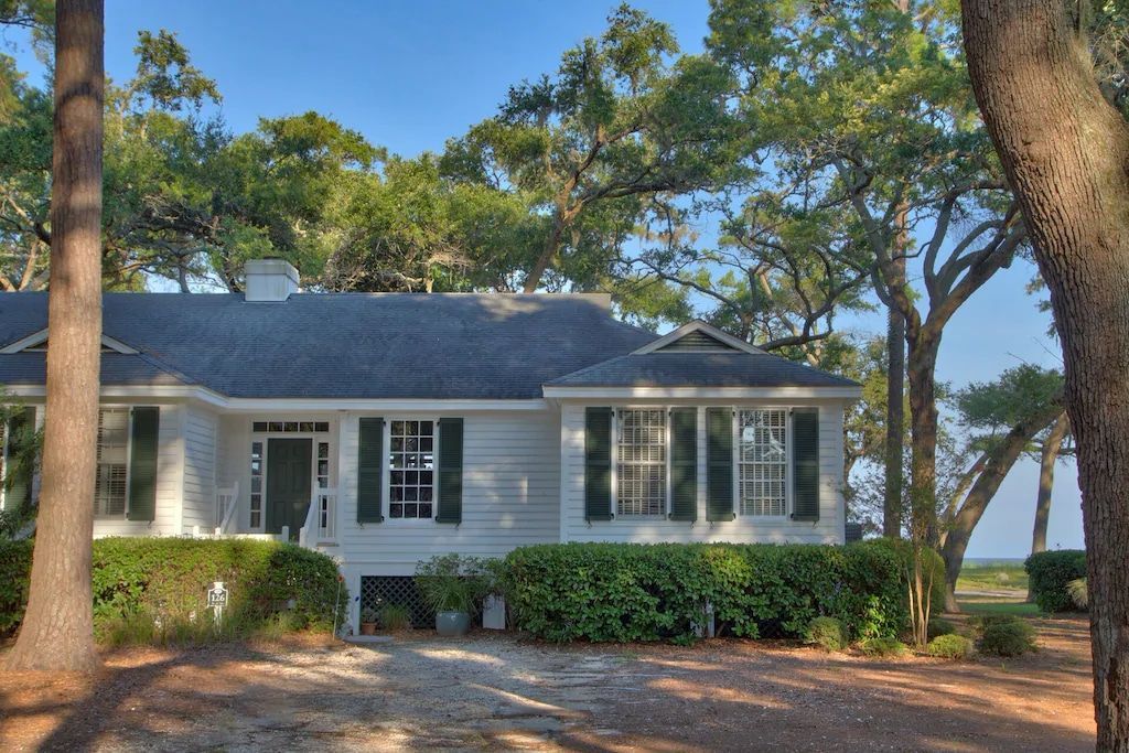 A white house with black shutters is surrounded by trees