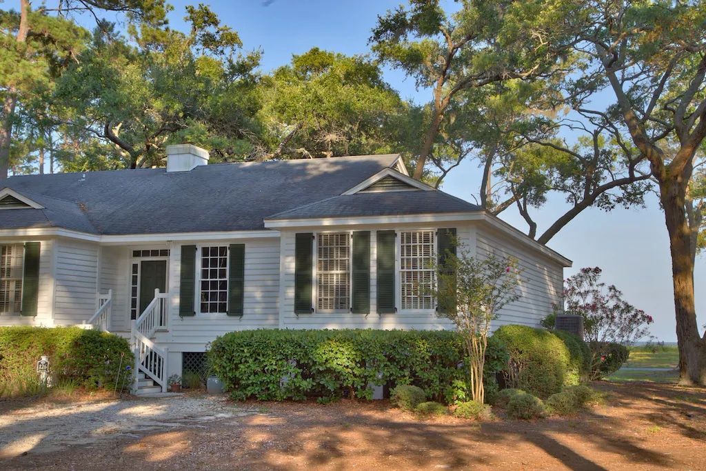 A white house with black shutters is surrounded by trees and bushes.