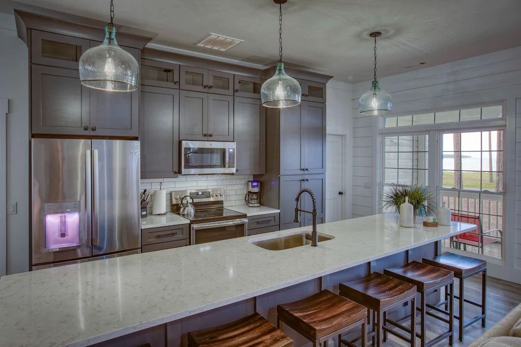 A kitchen with stools , a sink , a refrigerator , and a large island.