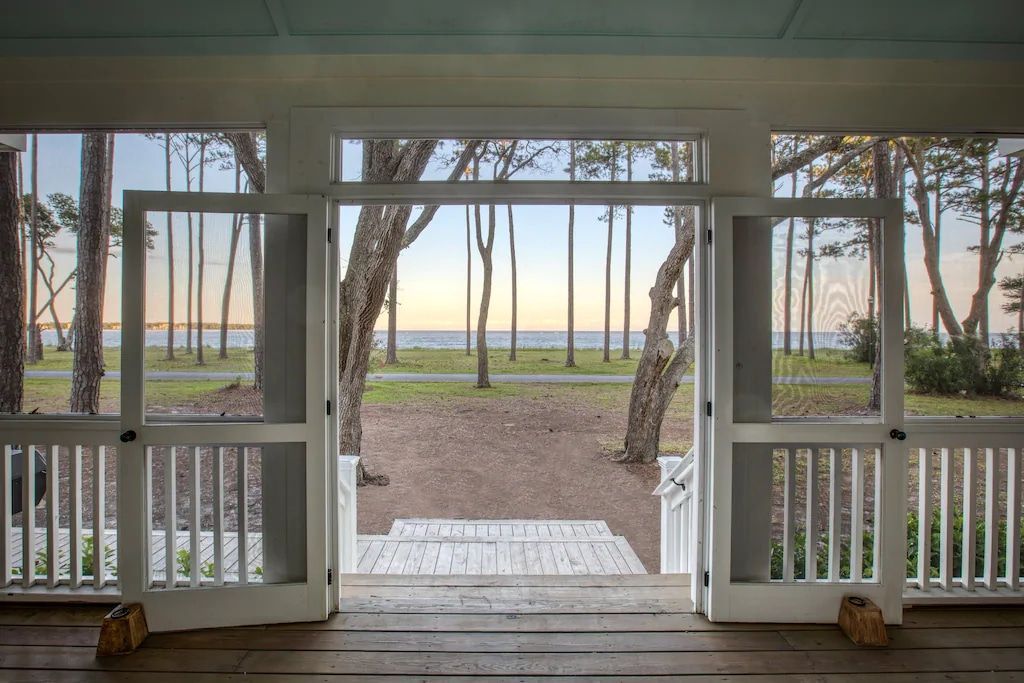 A screened in porch with a view of the ocean and trees.